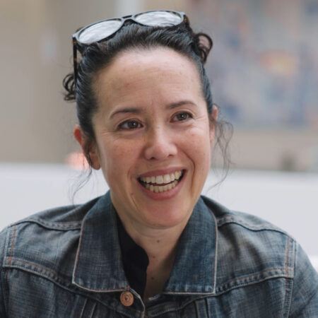 Sarah Sze with glasses pushed on top of her head, smiling looking out at the camera.