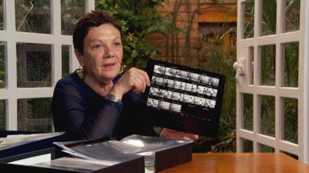 Graciela Iturbide sitting at a table with a photo box, holding up a sheet of negatives.