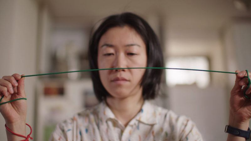 Aki Sasamoto holding a green elastic wrapped tight around her hands and in front of her face. 