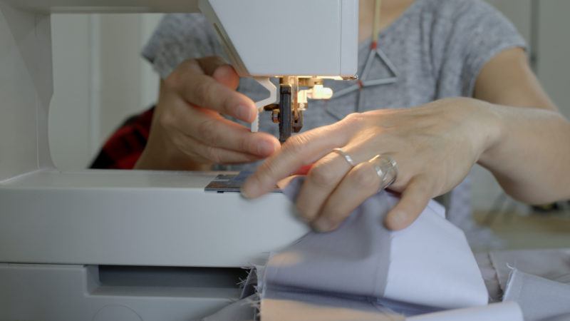 A person using a sewing machine to stitch fabric, with their hands guiding the material under the needle.