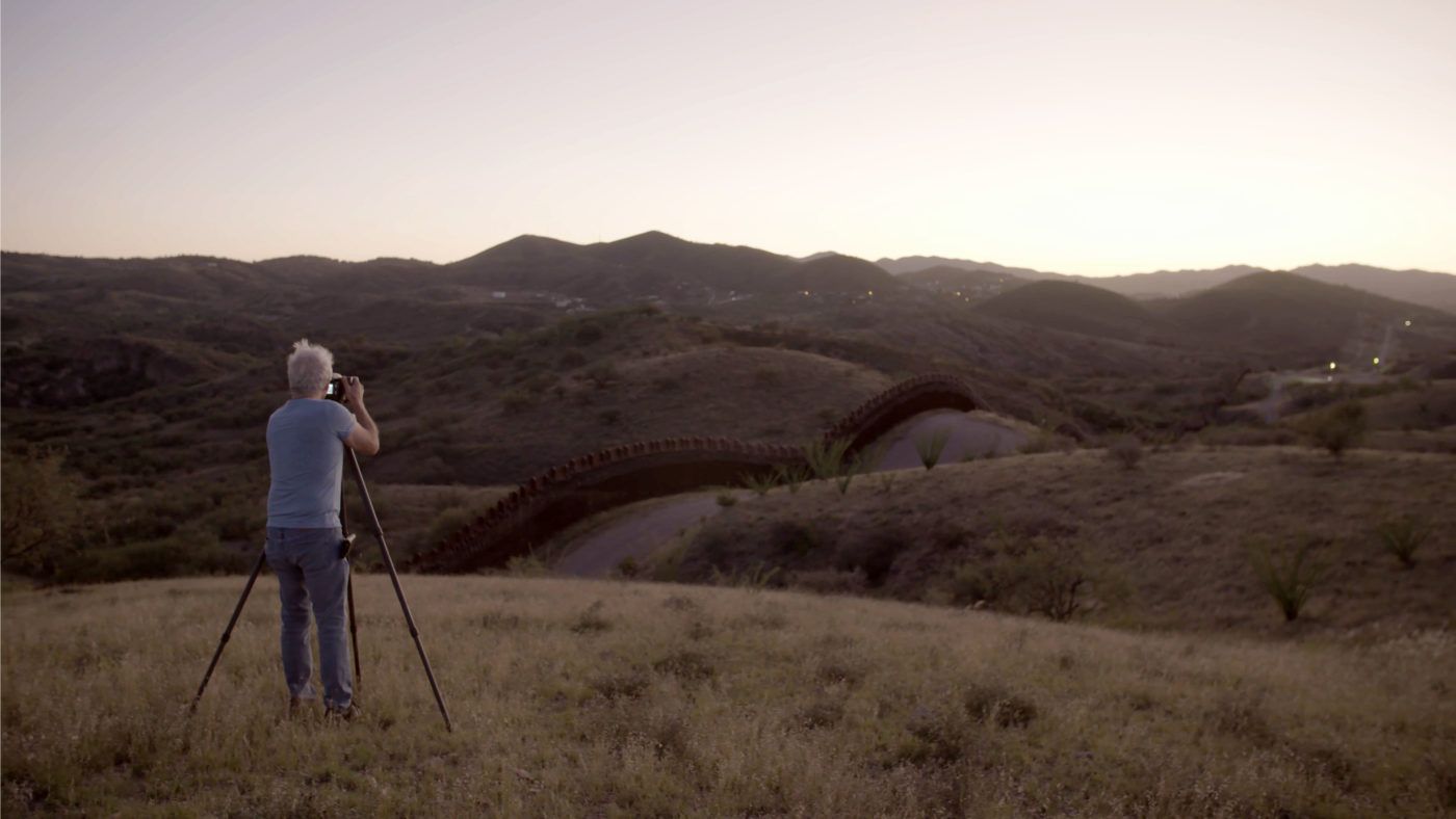 Richard Misrach standing on a hill photographing at the U.S.-Mexico border.