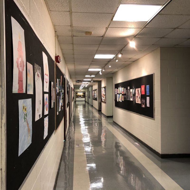 Photo of a school hallway devoid of human presence, with student artwork lining the bulletin boards along the walls