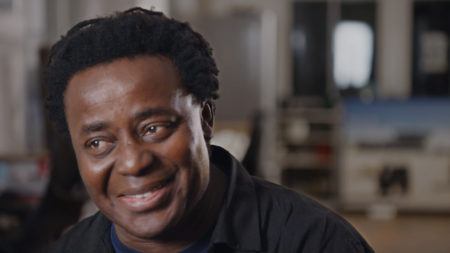 John Akomfrah smiling with head tilted down looking off camera.