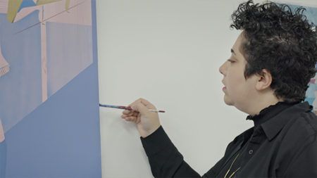Maryam Hoseini wearing all black, using a small paintbrush to paint the side of her canvas.
