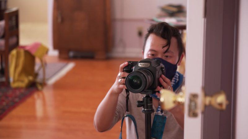 Tommy Kha holding a camera on a tripod focusing on capturing a shot through a doorway.