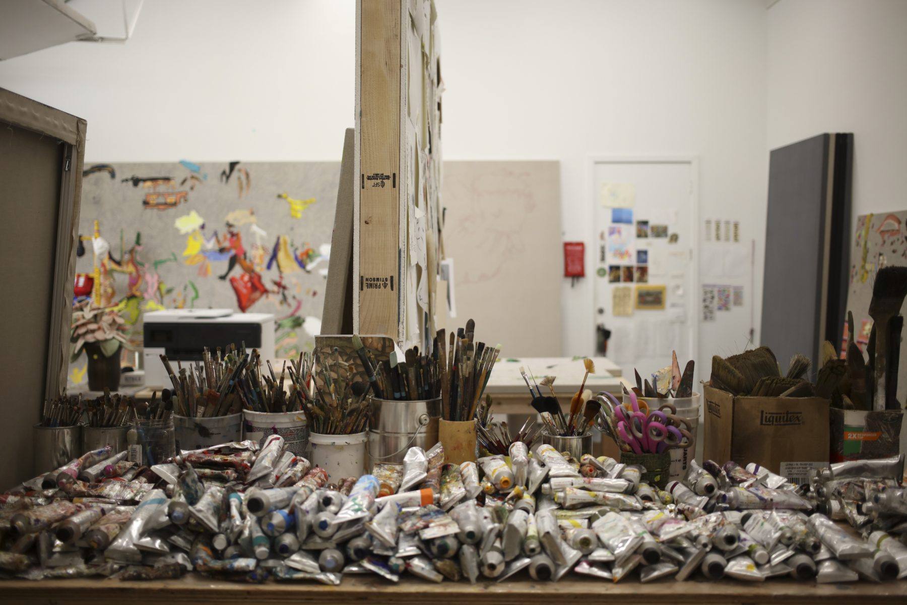 In Cindy Phenix's studio tubes of paint are piled upon one another in the foreground, with paintbrushes, canvases, and other painting materials within the frame.
