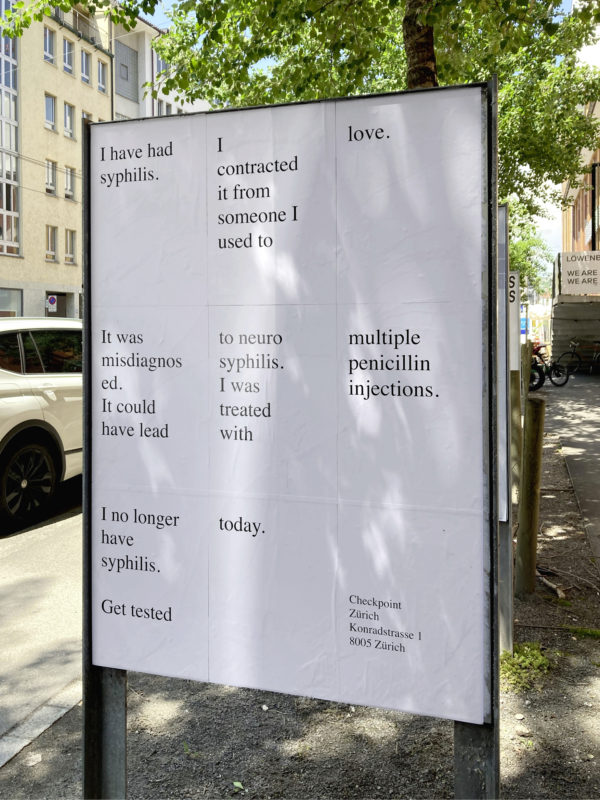 A white sign with black text stands outside in the shade. The text reads "I have had syphilis. I contracting it from someone I used to love. It was misdiagnosed. It could have lead to neurosyphilis. I was treated with multiple penicillin injections. I no longer have syphilis. Get tested today."