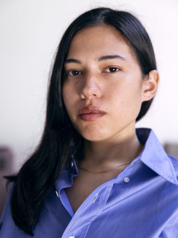 A headshot of artist Rose Salane wearing a blue button down with her hair down, swept to the right over her shoulder.