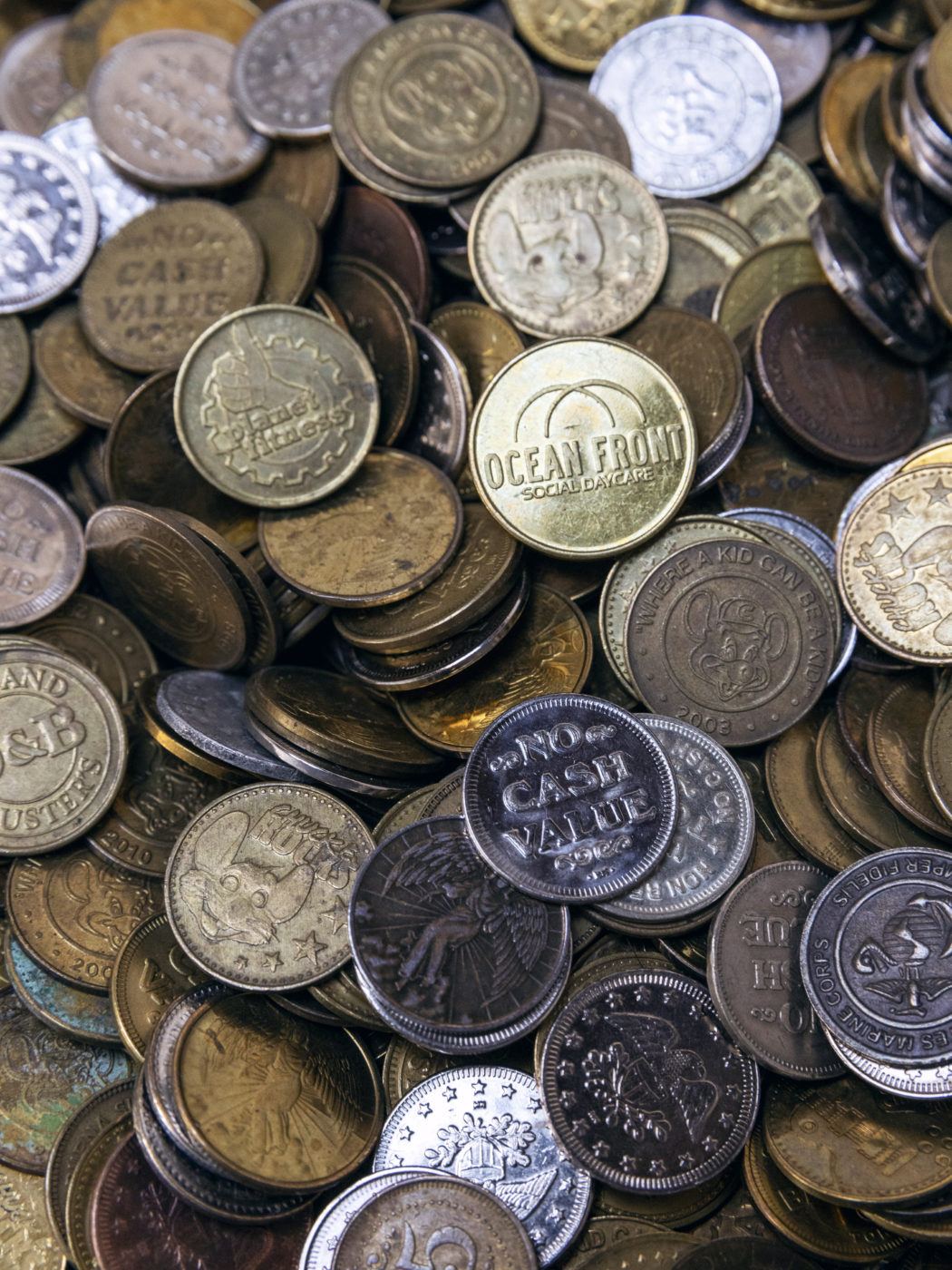 A close up image of pile of "slugs," the term used for objects used to trick MTA fare collection machines, some texts on the various coins read: "Ocean Fruit" or "Cash Value," alongside other words and phrases.