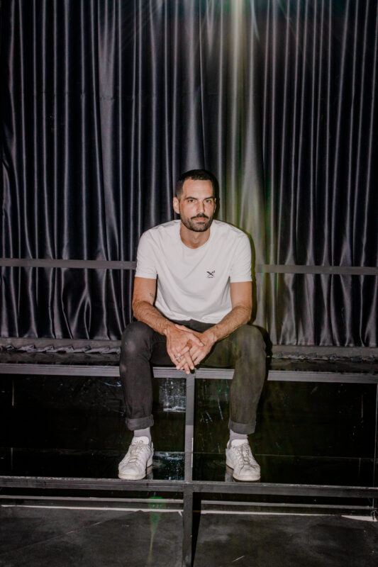 Artist Haig Aivazian sitting on a raised stage, looking into the camera.