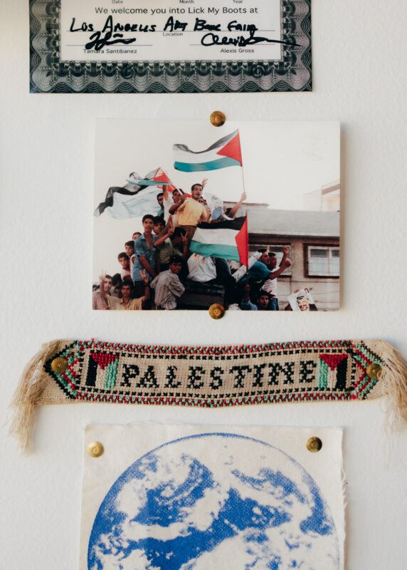 Close up of Jordan Nassar's studio wall featuring a photo of children waving Palestinian flags, above a cross-stitched fabric piece with 'Palestine' on it.