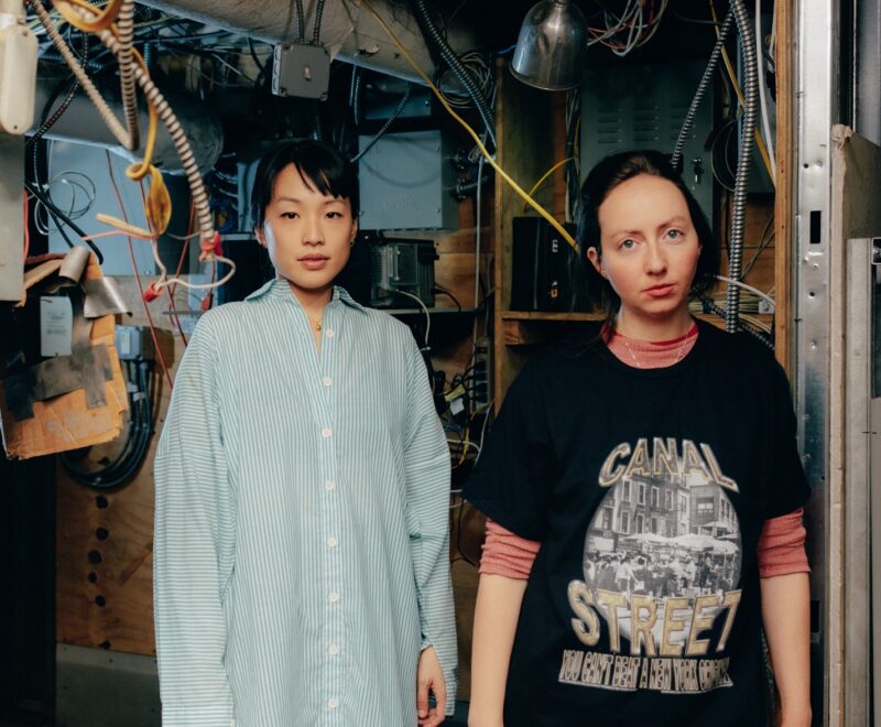 Ming Lin and Alex Tatarsky standing in their basement studio, wires and cords hang down on their heads.
