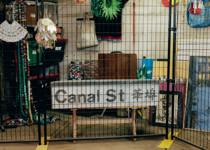 Shanzhai Lyric's studio with a "Canal Street" street sign and other items on the floor behind a metal grate fence.