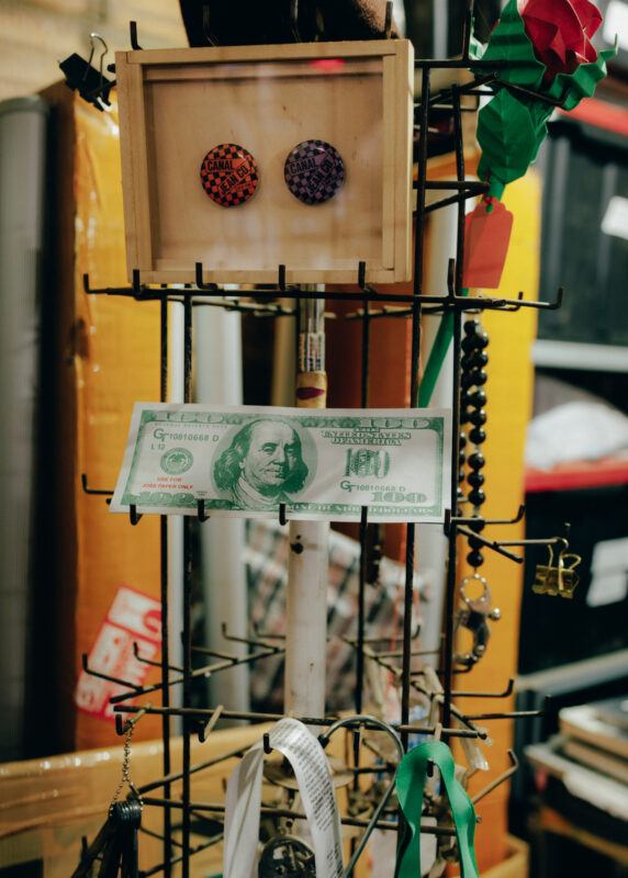 Close up of a jewelry stand hold different objects in Shanzhai Lyric's studio, including buttons, key rings, and a fake $100 bill.