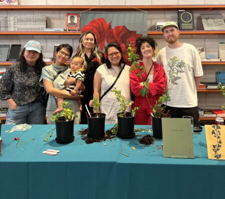 Group of Atomic Terrain members standing in front of a blue clothe covered table with four plants in black pots.