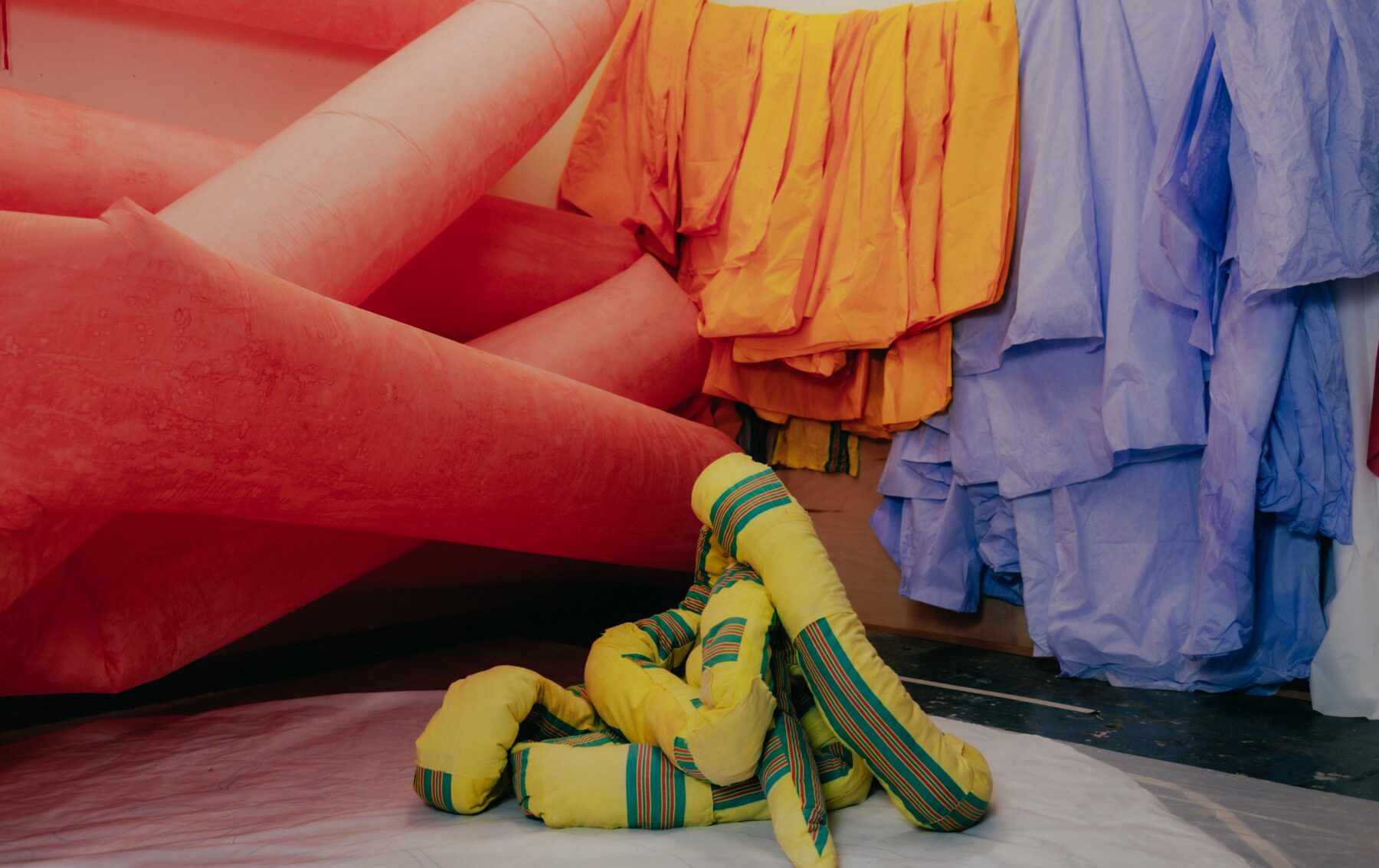 Colorful fabric pieces hanging from the walls, surrounding an inflatable yellow fabric sculpture arranged on the floor.
