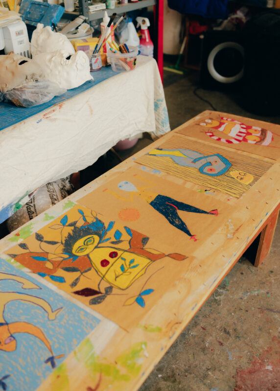 A wooden table in the studio with several drawings on brown paper laid across it.