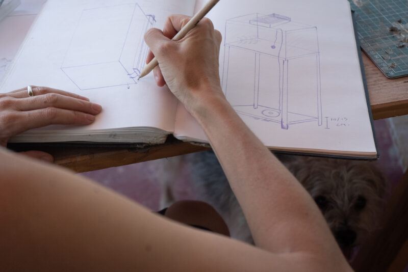 Person drawing furniture sketches in a notebook at a desk.