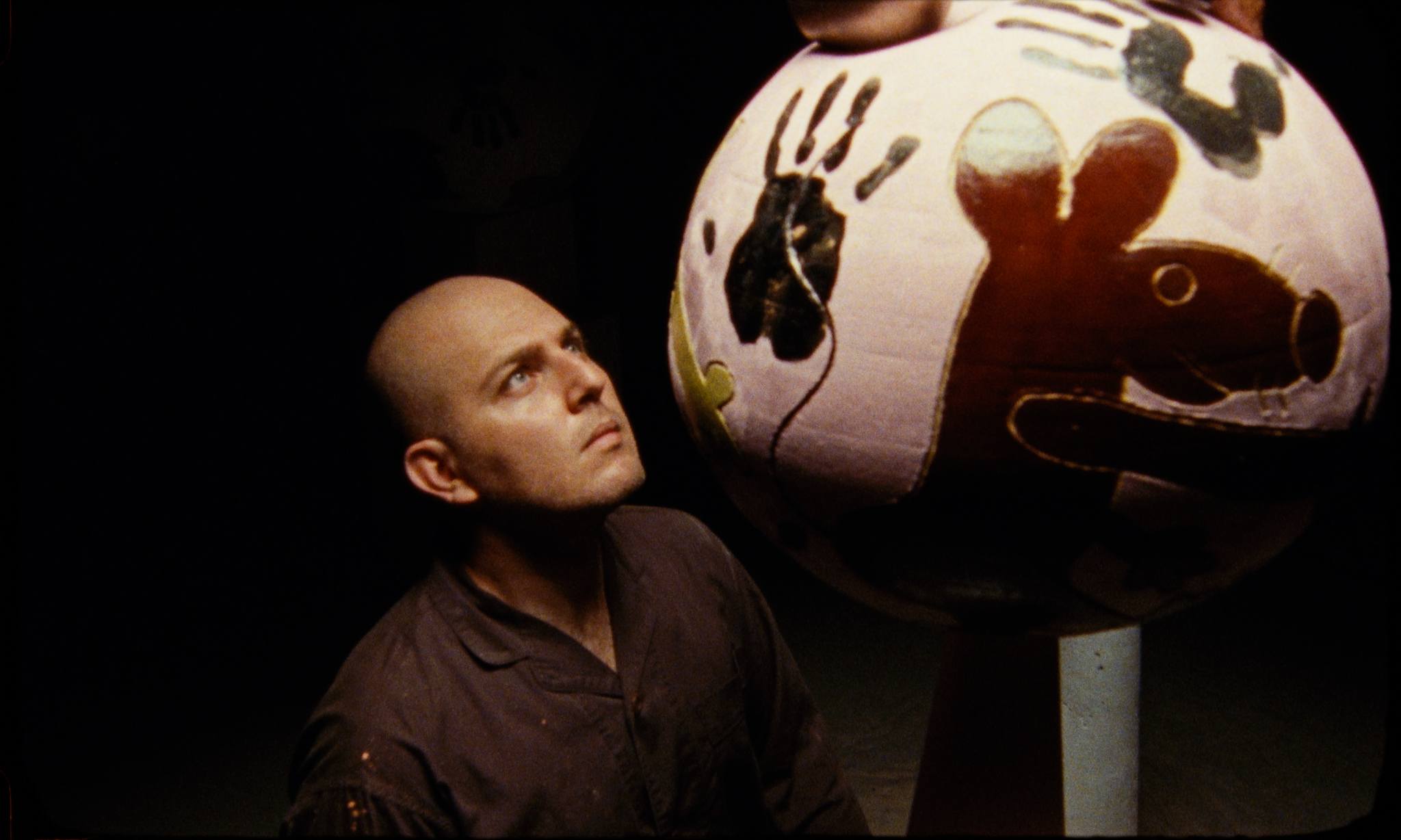 Hadi Falapishi looks up at a large, painted ceramic with animal and hand designs in a dimly lit space.