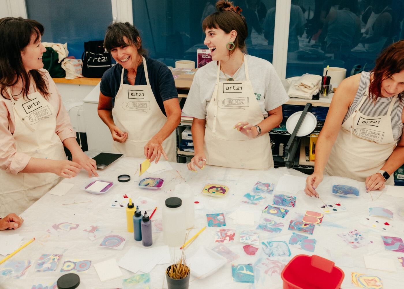 Four people in aprons engaged in a group art activity, surrounded by colorful paper and art supplies on a table.