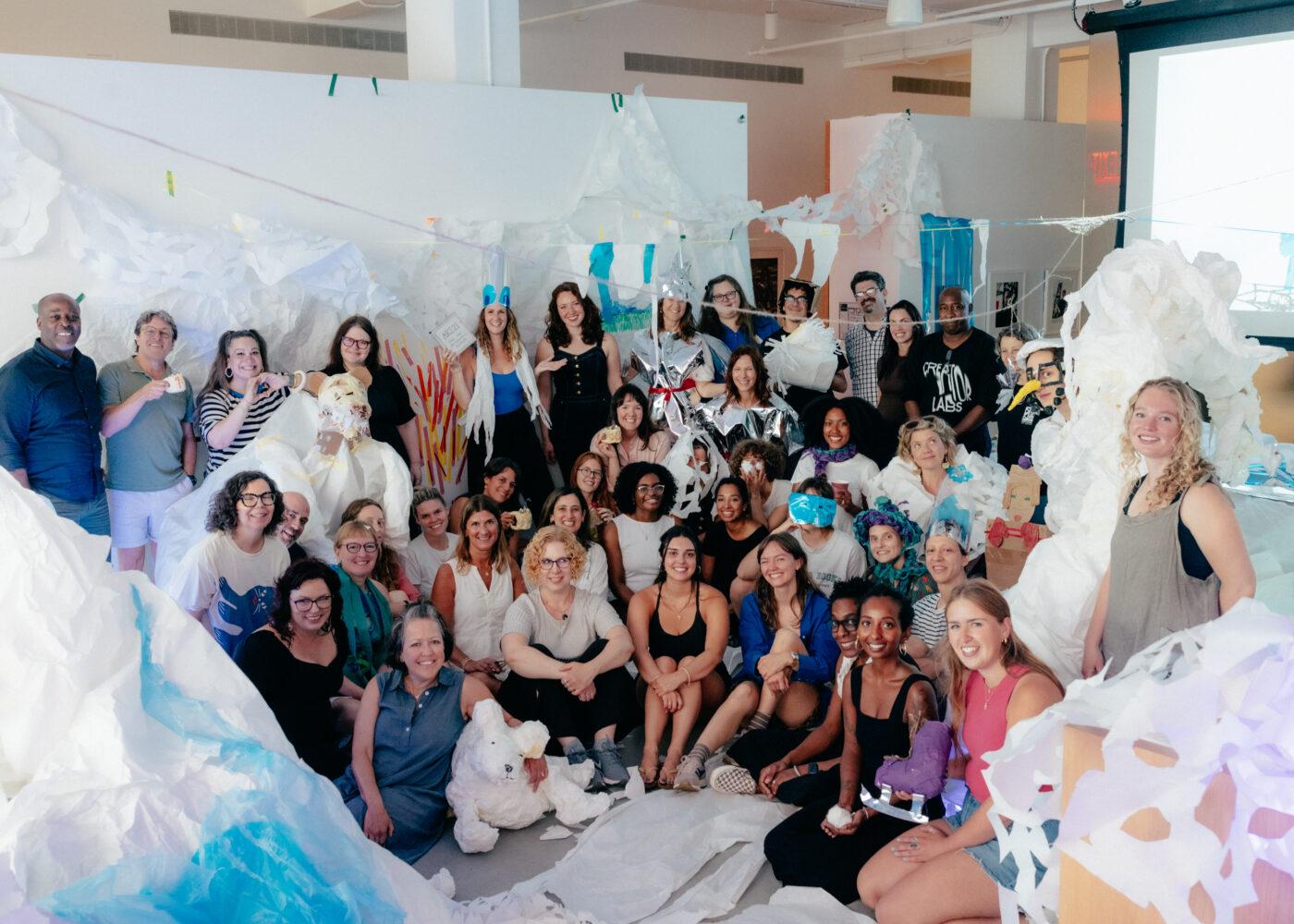 A large group of people posing together in a room decorated with snow made out of white and blue papers.