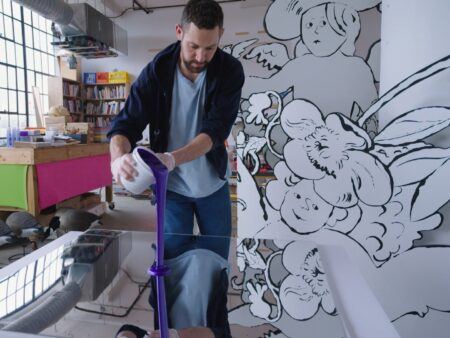 Alex Da Corte pours purple paint onto a reflective surface in an art studio.