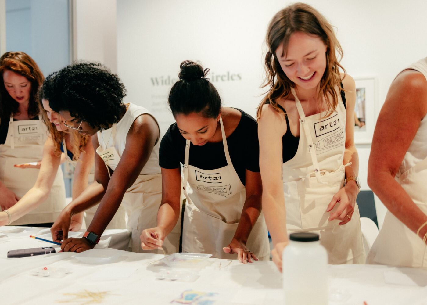 Group of people in canvas aprons engaged in an art project at a table.