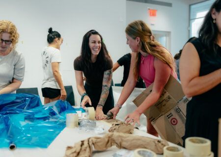 People working together on a project involving blue plastic sheets and packing materials at a table indoors.