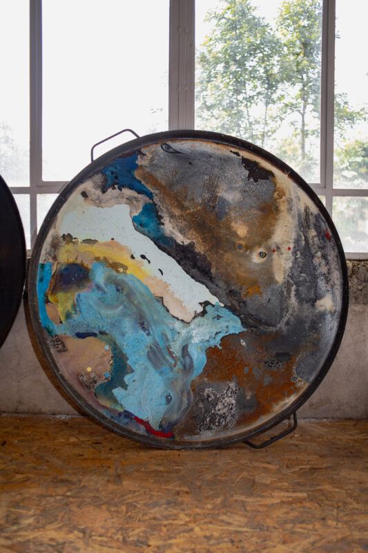 Large, colorful abstract artwork on a circular metal tray displayed upright in front of a window.