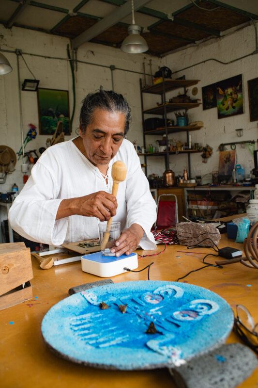 Fernando Palma Rodriguez works on a blue sculpture in a workshop filled with artistic tools and materials.