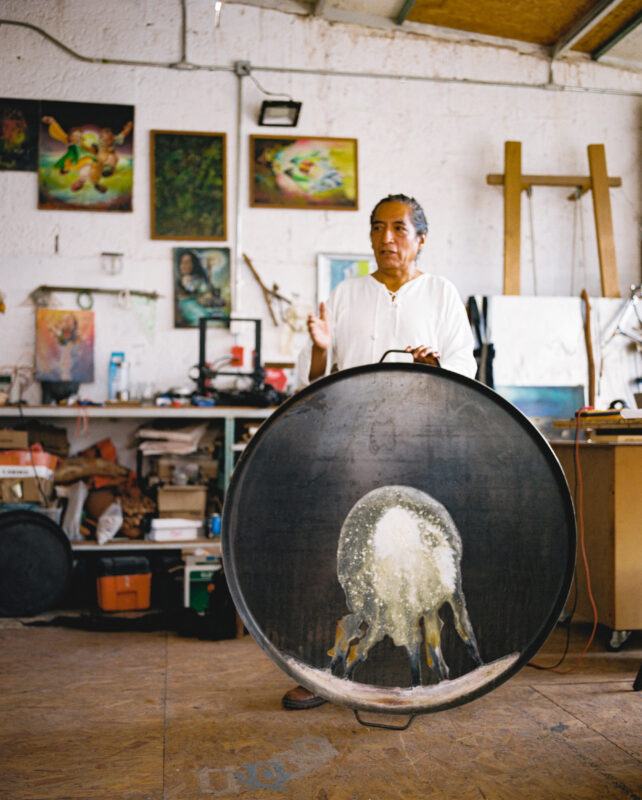 Fernando Palma Rodríguez stands in his studio holding a large, circular artwork featuring an intricate design.