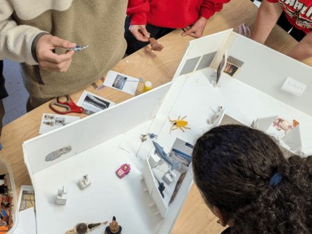 Students gathered around a table working on a scale model project with miniatures and cutouts on it.