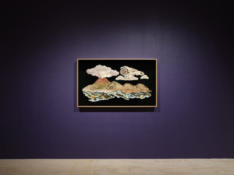 Framed landscape artwork with mountains, clouds, and a sun displayed on a dark purple wall in a gallery setting.