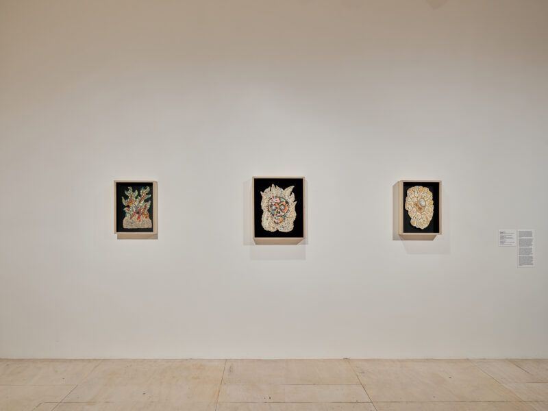 Three framed artworks on a white gallery wall, each featuring intricate, abstract patterns on a black background.