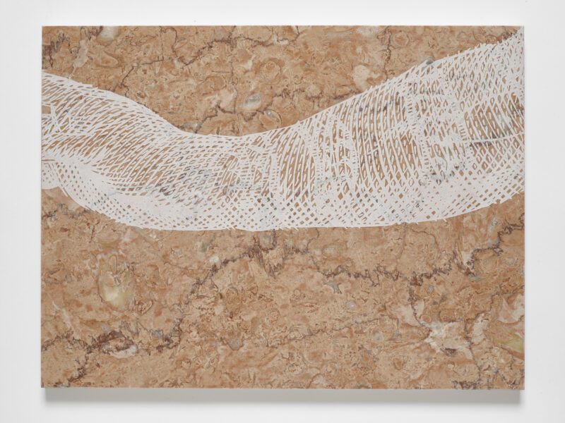 A beige and brown marbled surface features a white, intricate arm, cut off at the fingers.