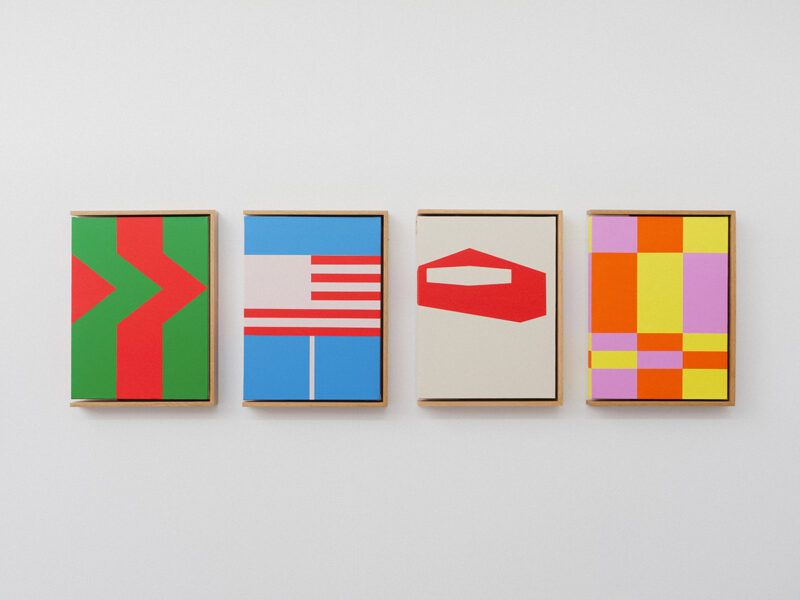 Four colorful abstract geometric paintings in rectangular frames hanging on a white wall in a row.