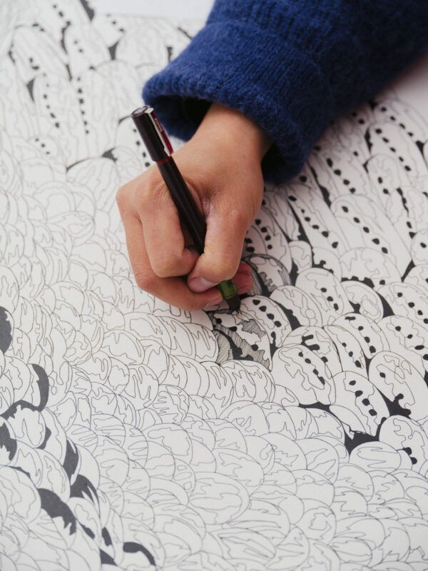 Hand holding a pen, drawing intricate black patterns on a white sheet.