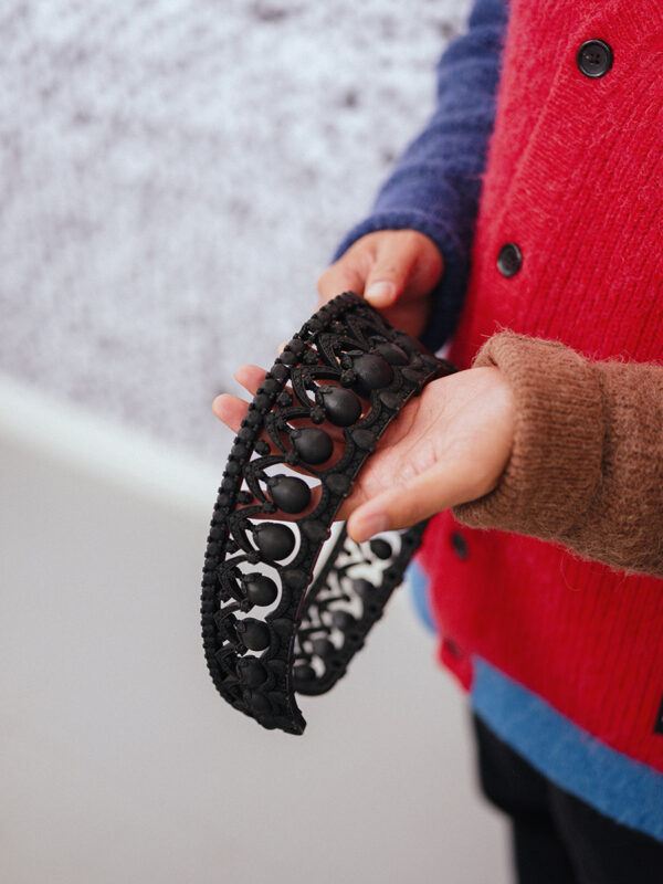 Close up of a person wearing a red and blue sweater, holding a black, intricately designed headpiece.