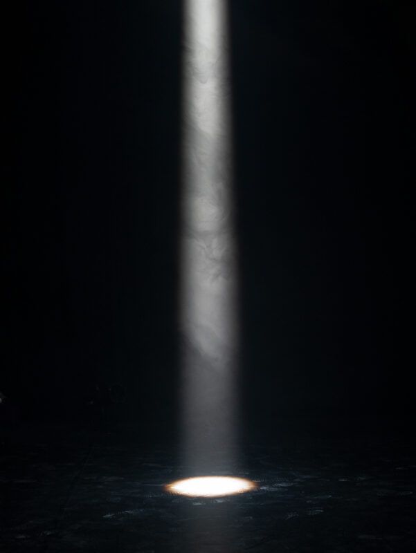 A focused beam of light illuminates a circular spot on a dark stage or floor, creating a spotlight effect in an otherwise dimly lit environment.