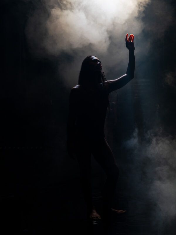 Silhouette of a person reaching up with one hand, surrounded by smoke and illuminated by light from above.