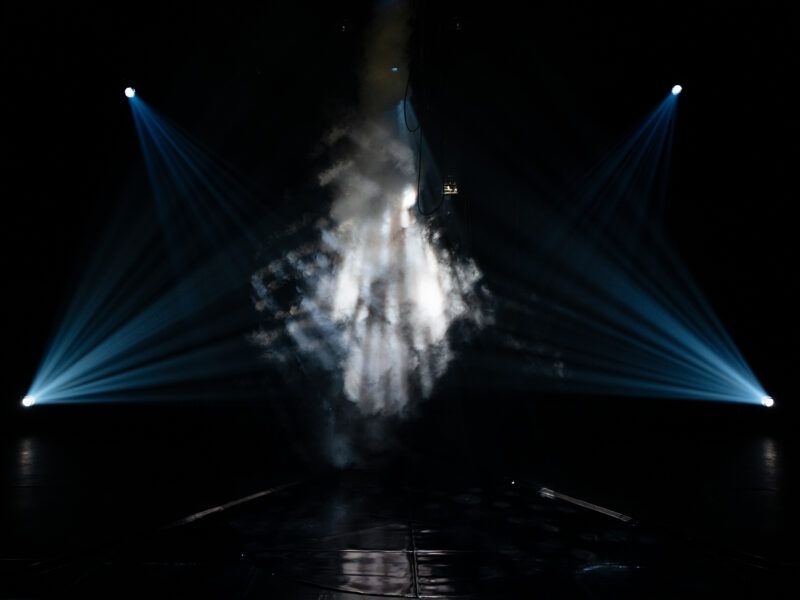 A dark stage with blue spotlights beams and smoke creating a dramatic, atmospheric effect.