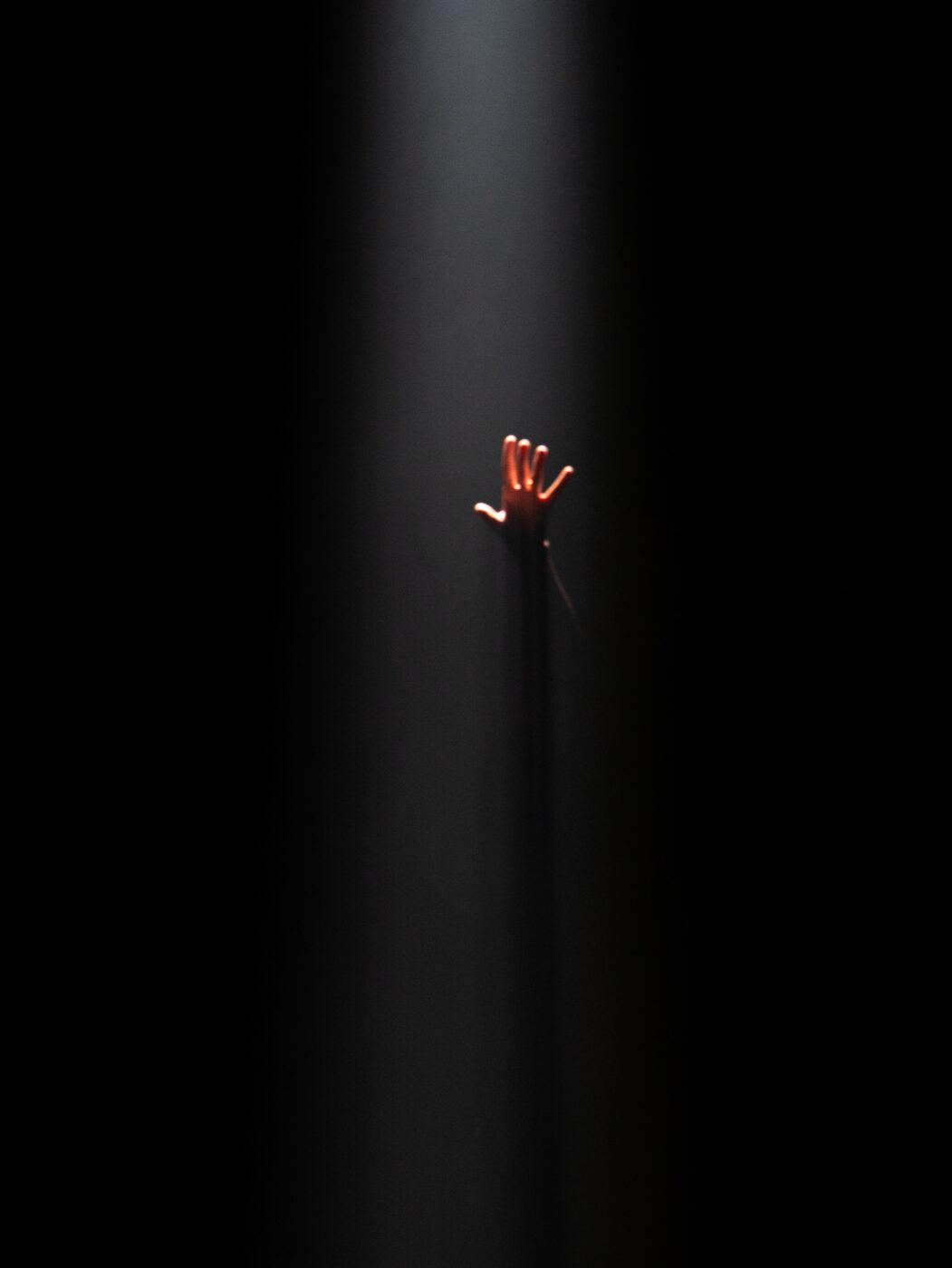 A solitary hand reaches upward into a beam of light against a dark background.