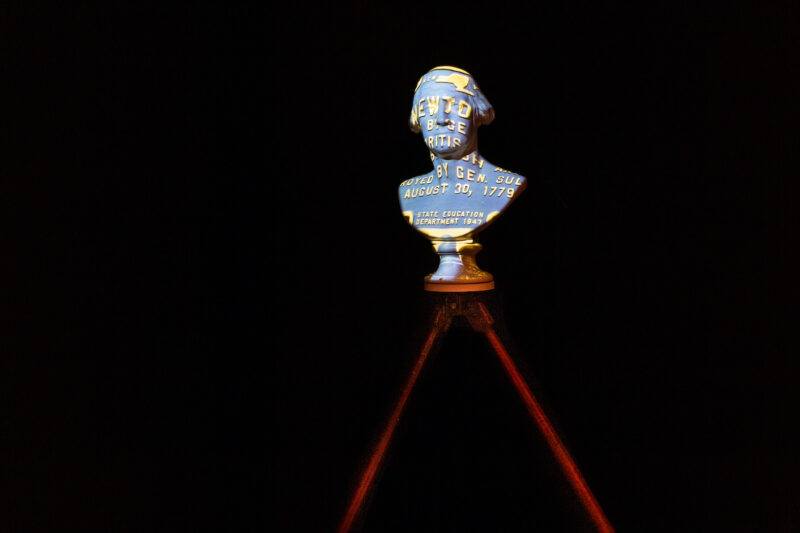 A bust with text projected on it stands illuminated against a dark background on a tripod.