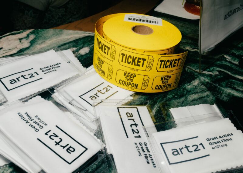 A roll of yellow tickets labeled "Keep This Coupon" sits on a marble surface next to several packaged Art21 promotional items.