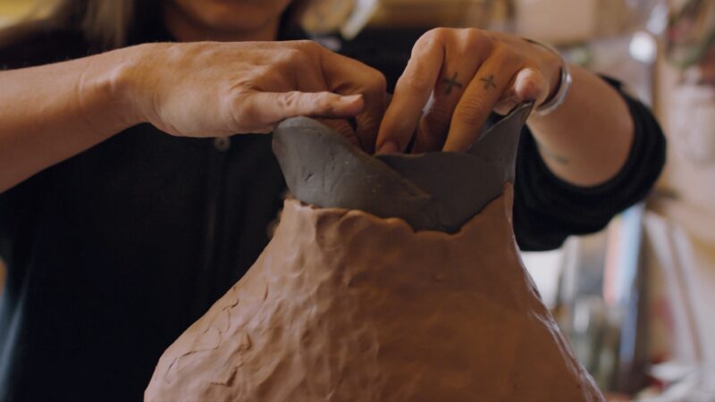 Close-up of a person shaping the rim of a clay vase with their hands.