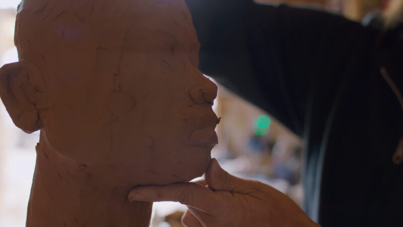 A person sculpts a human head out of clay, gently shaping the chin with their fingers.