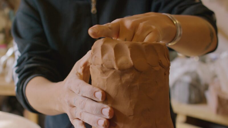 Hands shaping a brown clay object, with careful pressure and technique.