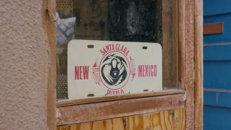 A license plate with "Santa Clara Pueblo" and "New Mexico" is displayed in a window, featuring a black logo in the center.