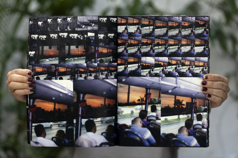 Hands holding an open photo book showing multiple images of people on a bus and a sunset outside the bus window.