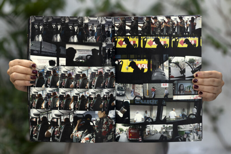 Hands holding open a photo book displaying multiple candid street and urban scene photographs, shown in a grid layout.